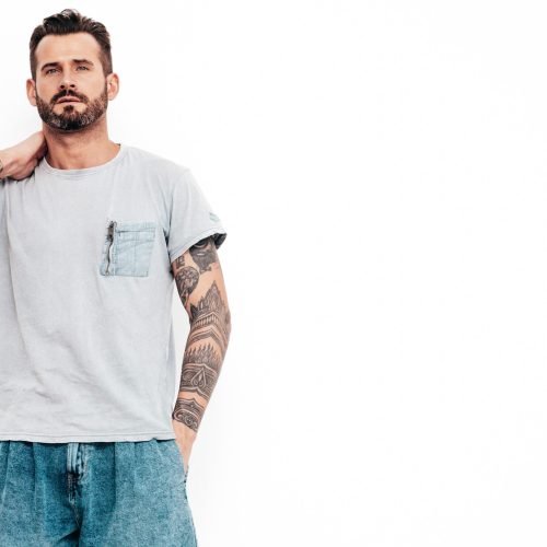 Portrait of handsome confident stylish hipster lambersexual model. Sexy man dressed in T-shirt and jeans. Fashion male isolated on white wall in studio