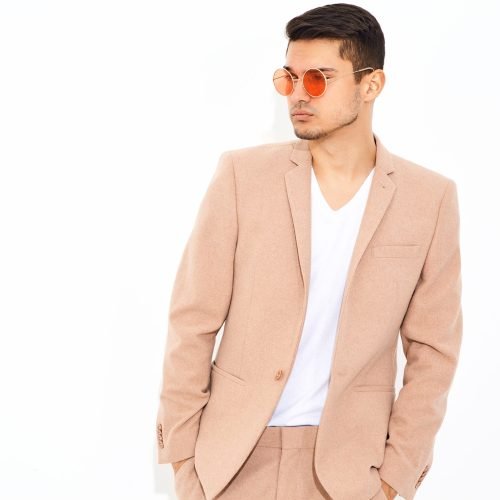 portrait of handsome fashion stylish hipster lumbersexual businessman model dressed in elegant light pink suit posing near white wall in studio. Metrosexual